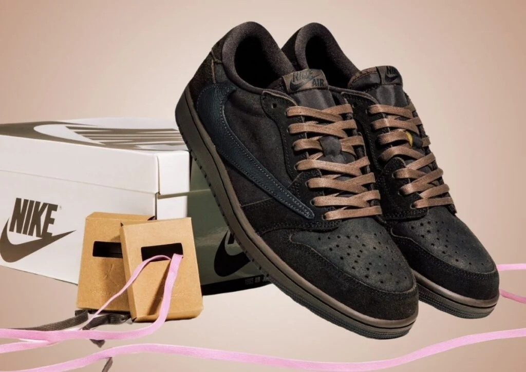 Travis Scott x Air Jordan 1 Low OG "Velvet Brown" avec détails en cuir premium, swoosh inversé et lacets alternatifs rose et marron, posée devant une boîte Nike.